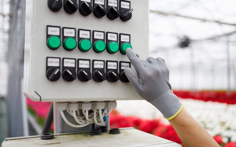Close-up of a flower greenhouse worker's hand in a glove pressing a button on the control panel